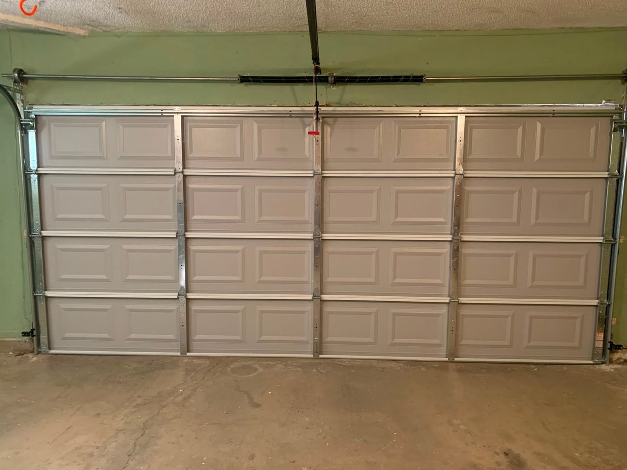 Short-panel steel garage door installed with new track and torsion spring, viewed from inside the garage